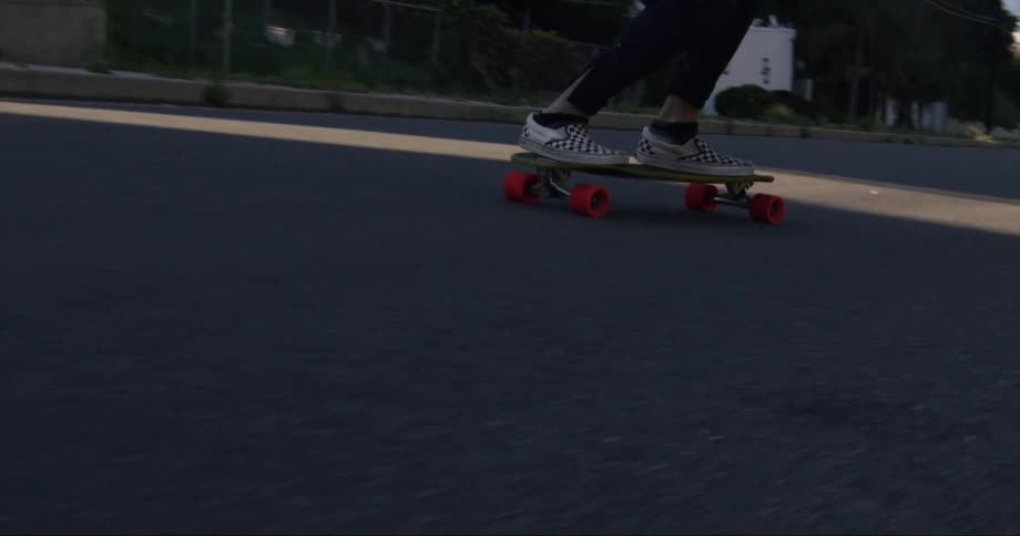 Skateboarder wearing checkered vans riding downhill on a neighborhood street
