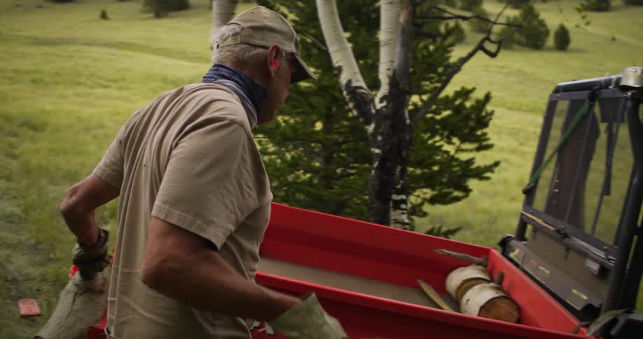 A man carries chopped sections of thick tree branch to place them in the bed of an offroad vehicle