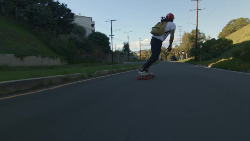 A teenage boy wearing a backpack is riding his skateboard on a neighborhood street