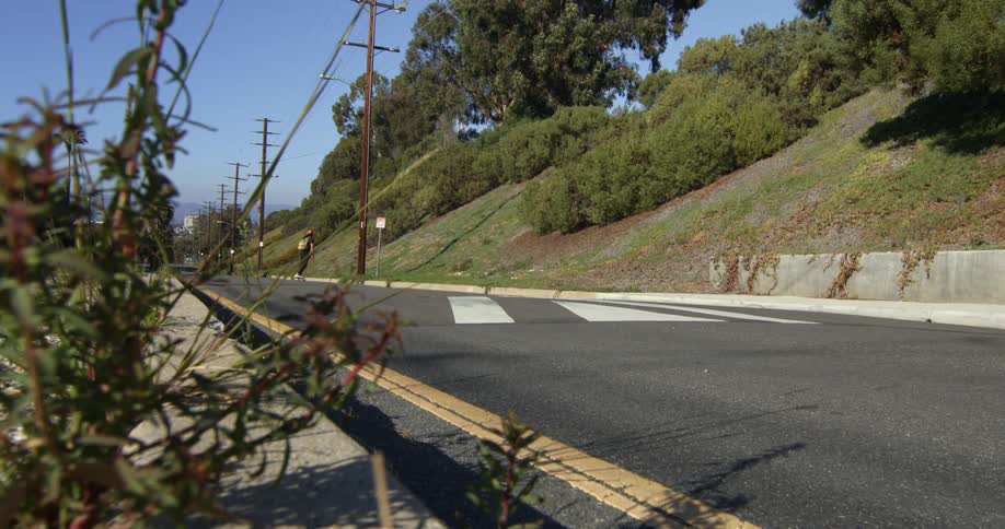 A teenage boy wearing a backpack is coasting downhill on his skateboard on a neighborhood street