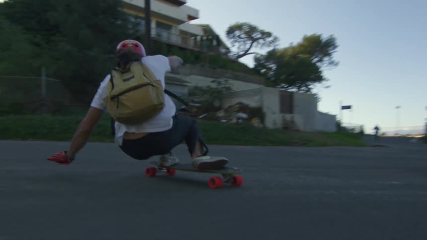 Skateboarder crouches on skateboard to turn sharply around island in middle of street near apartment buildings