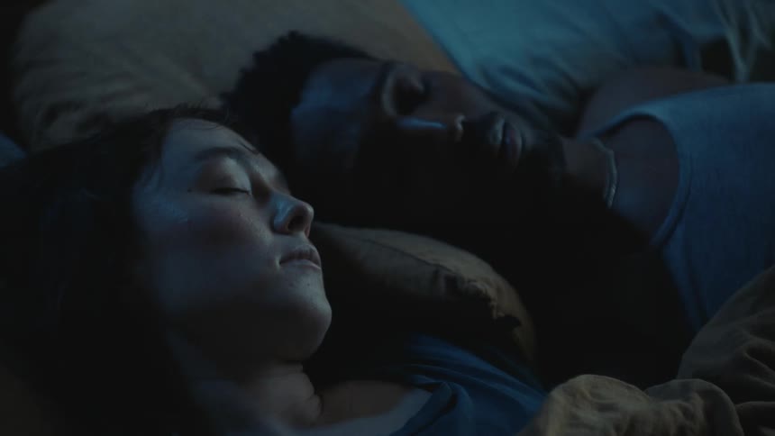 An interracial couple sleeping under blankets on a bed