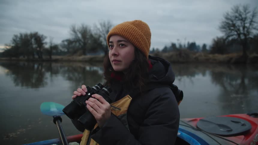 Woman sitting in kayak smiles while looking through binoculars