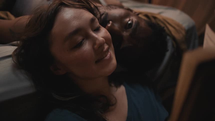 Woman reclined on the bed reads a book to her couple in the bedroom