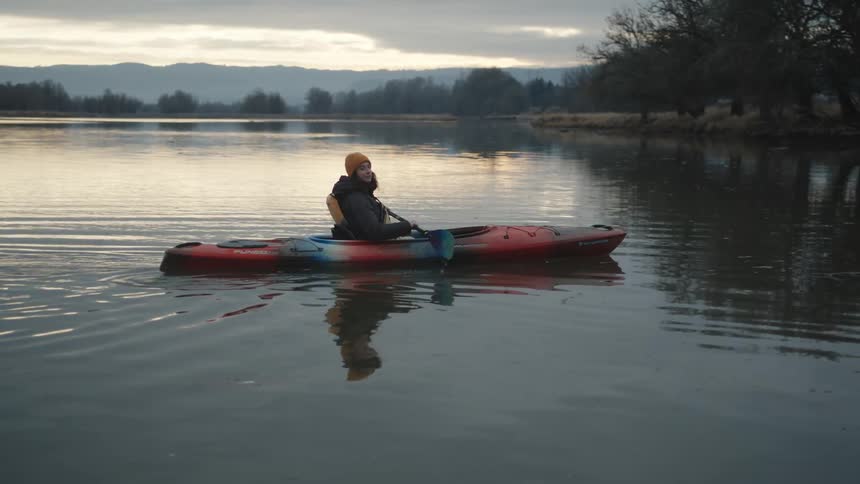A woman is kayaking in a lake at dusk