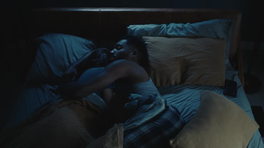 A man rolls over in bed and is pushed away by a woman