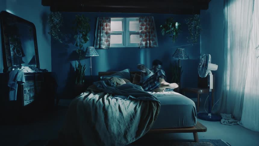 A man wakes up and turns the fan on