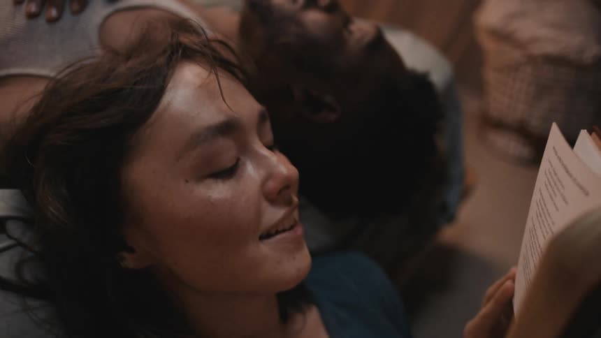 A female reading from a book to a male next to her