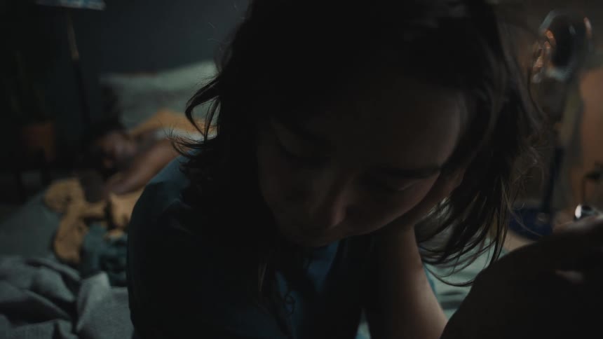 A man sleeping in bed as a female sits on the bed flicking a lighter