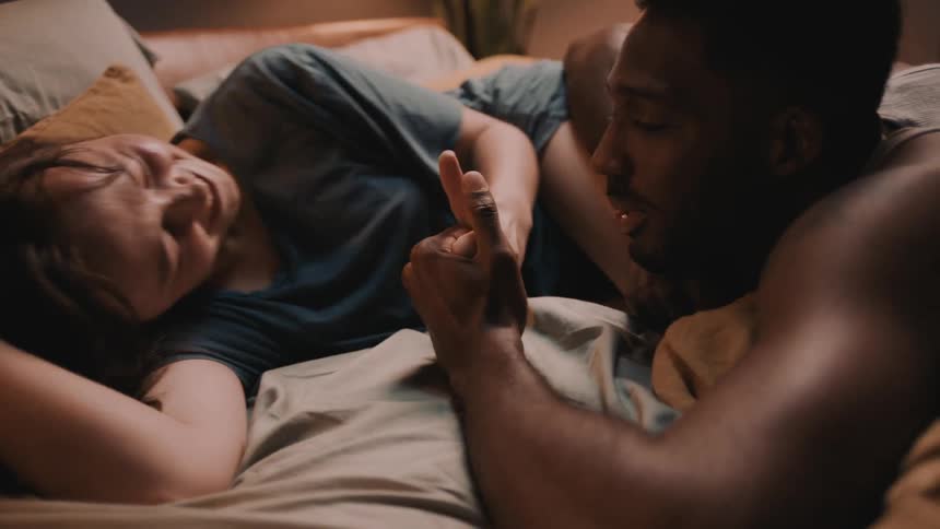 Couple smile while lying on bed playing thumb war