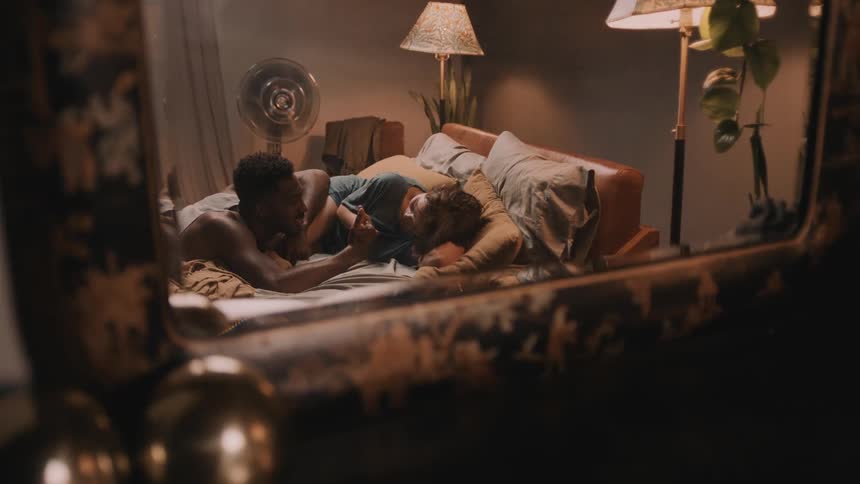 Couple lying on bed reflected in nearby mirror play thumb war