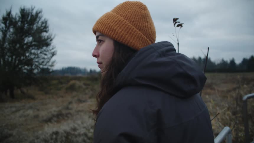 Woman wearing coat leans against rail on path and looks out toward horizon