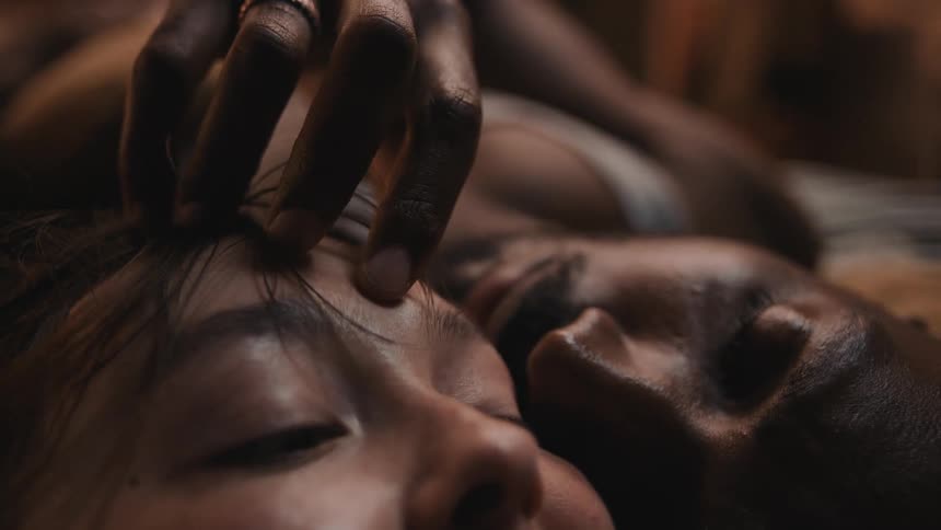 A man lovingly caresses his wifes face with his fingers while she playfully kisses them