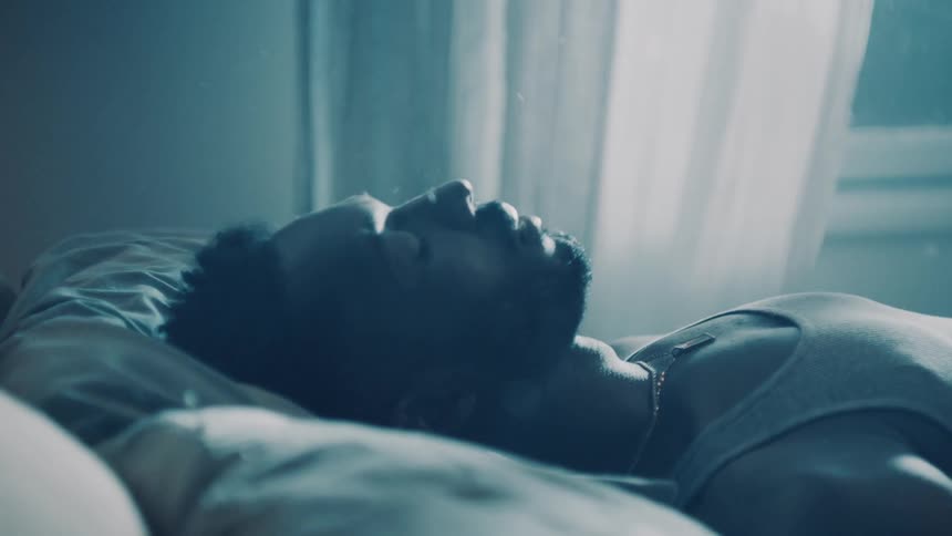 A man falls onto his bed with his eyes closed