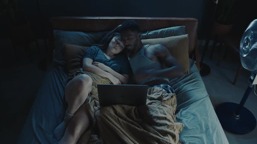 Couple wake up to watch funny media on laptop before going back to sleep