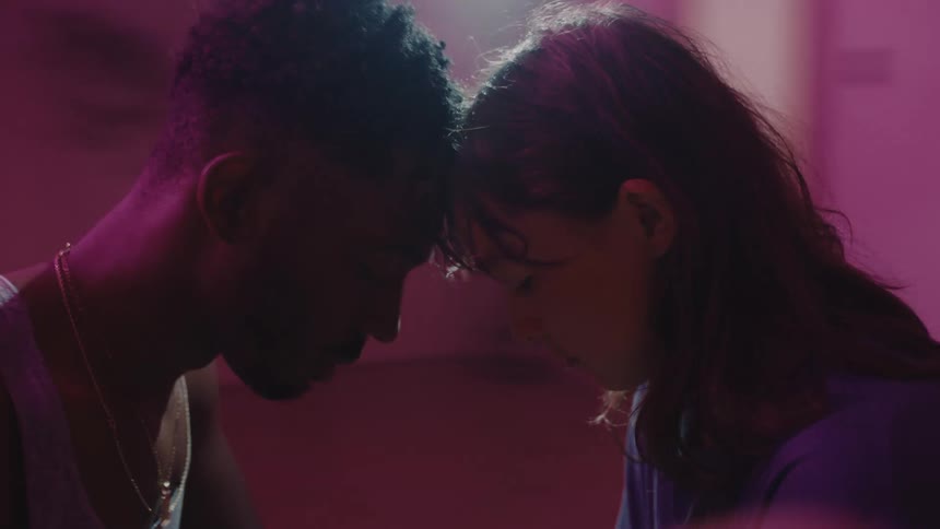 Surreal footage of a couple touching foreheads spinning inside a room under colorful lights