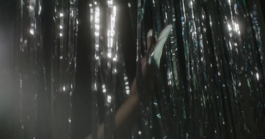 A hand running through metallic tinsel foil fringe curtains