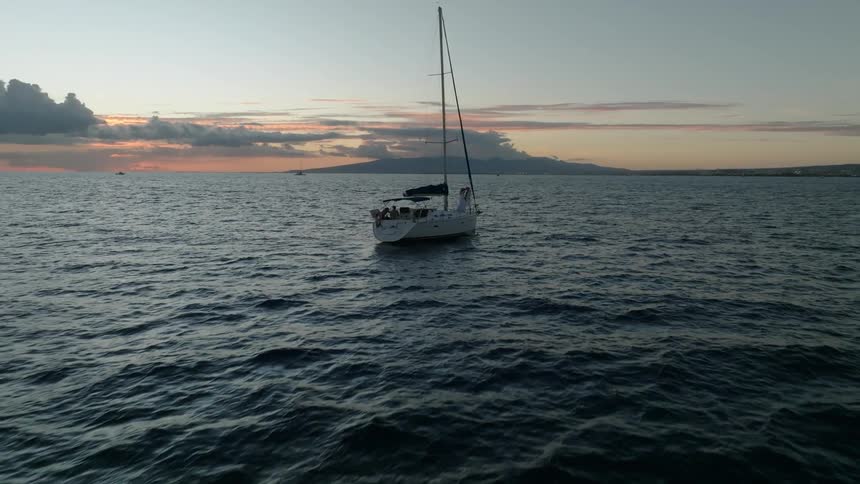A sailboat floating at sunset with a man and woman dancing and kissing on the bow deck