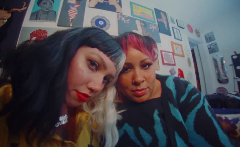 Two women with colorful hair sitting in a room looking at the camera