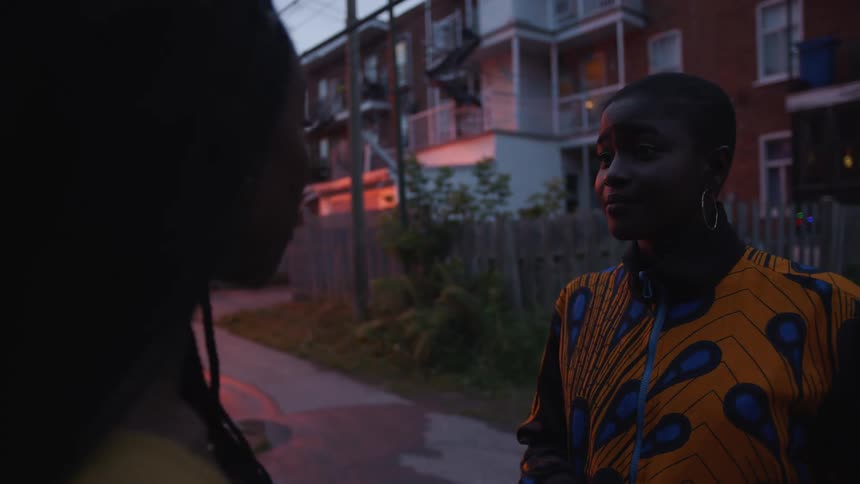 Two women stand in road near apartments at night talking
