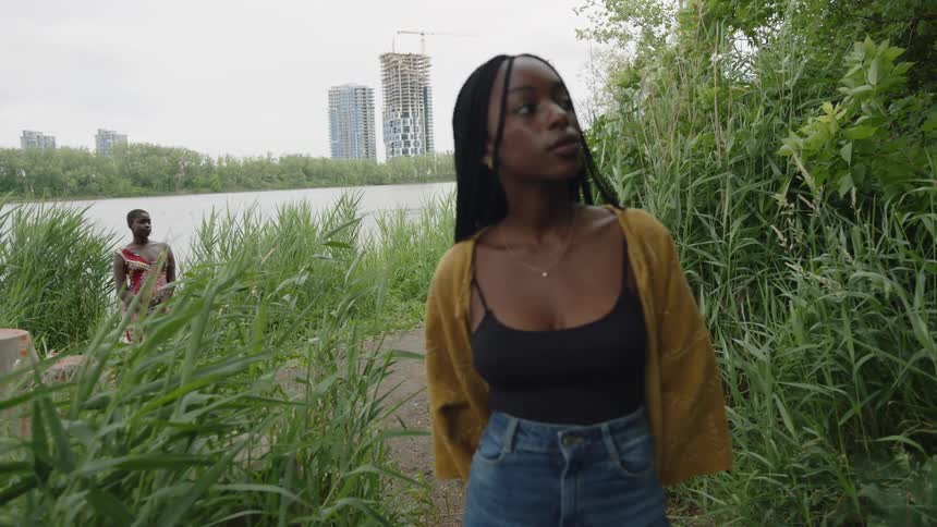 Young woman standing near a river on the outskirts of the city at daytime