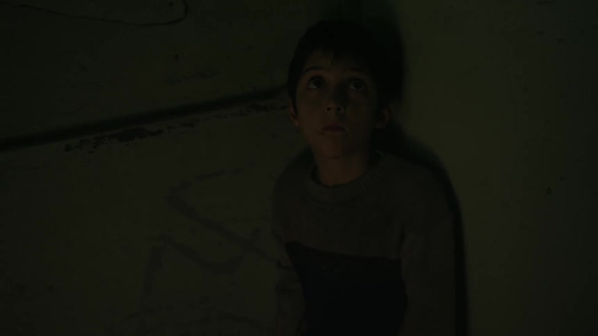 A boy hides in the corner of a dark room