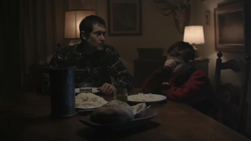 A father and son sit at a dark dinner table and get up suddenly after lightning crashes