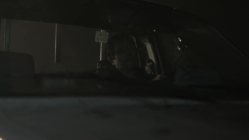 Man sitting on a car parked at night despondently throws an object over the dashboard