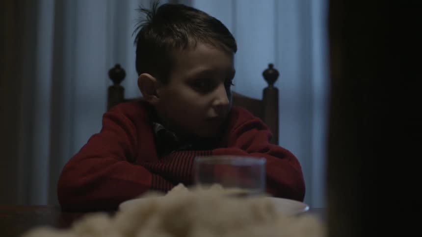 A boy sitting at the dinner table gets up
