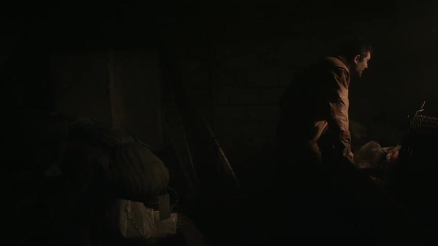 Light shines on a man standing in a dark cluttered room as he vigorously rubs his face with his hands