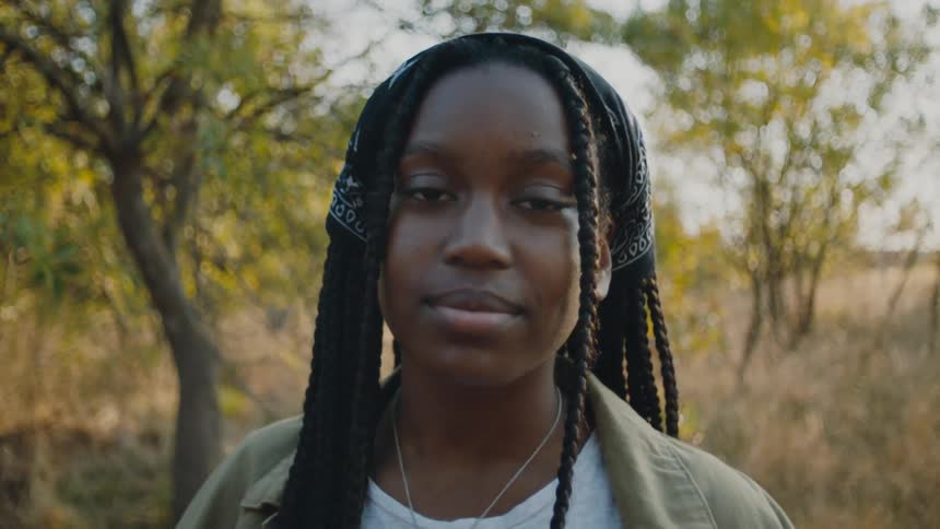 A teenage girl in a forest area turns her head to pose for a photo