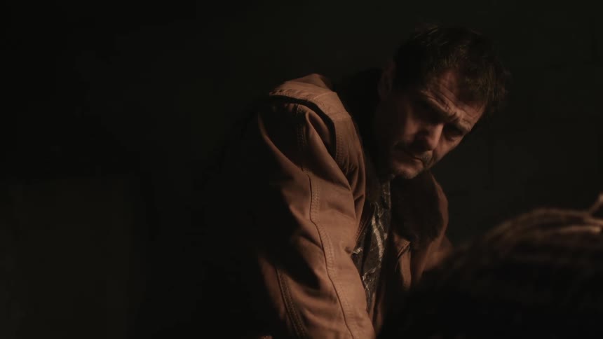 A man slowly holds his head up to stare at the camera