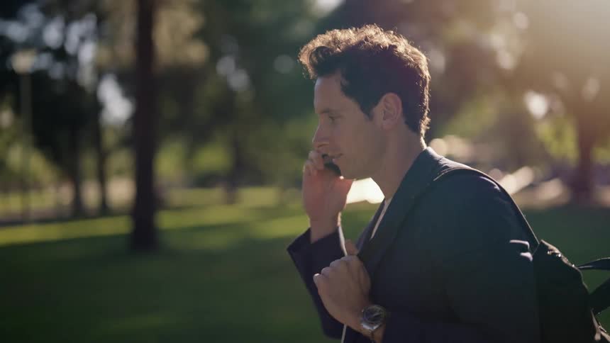 A man talking on smartphone removes the phone from his face to tap the screen while walking outdoors during the day