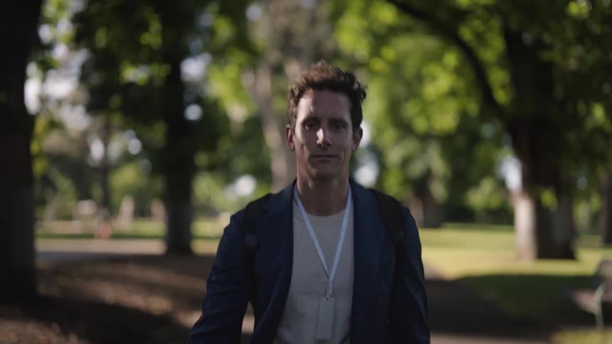 A man is walking through a park on a sidewalk lined with trees