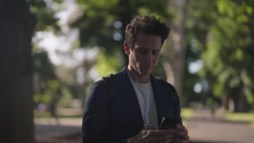 A younger white man is outside in the city and is on his phone