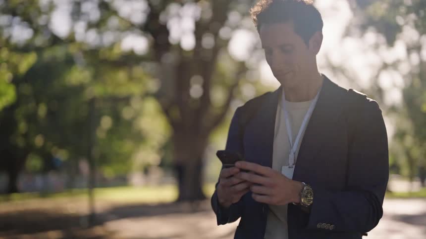 A man is typing on his phone in the park