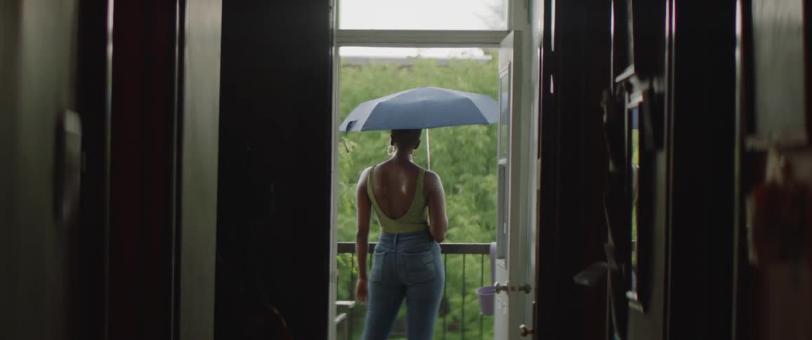 Woman with short hair hoop earrings low cut shirt and jeans holds umbrella on balcony overlooking green forest