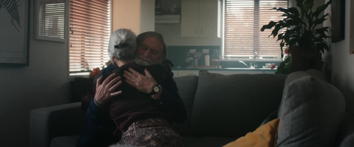 An elderly couple sitting on a couch hugging