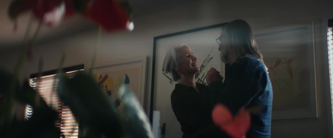 Man smiles and kisses woman as they slow dance at home