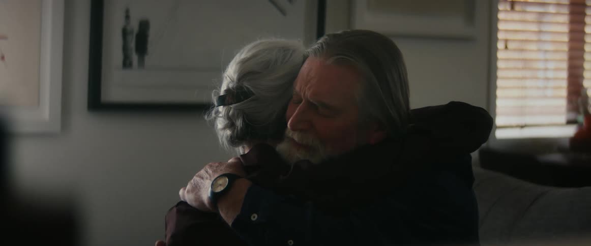 A woman leans forward and kisses her husband and they hug one another