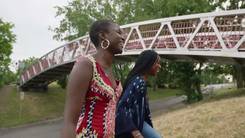 Two women laugh and talk while walking through the park