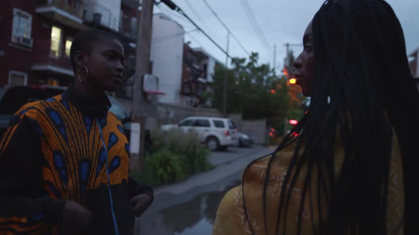 Woman with braids yellow jacket talks to woman with short hair and orange and black jacket on the street in the neighborhood in the city
