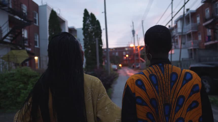 Two women are talking as they walk past apartments on a neighborhood street