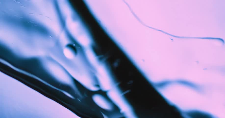 Blue and pink pastel light shines on a splashing liquid as bubbles float and move