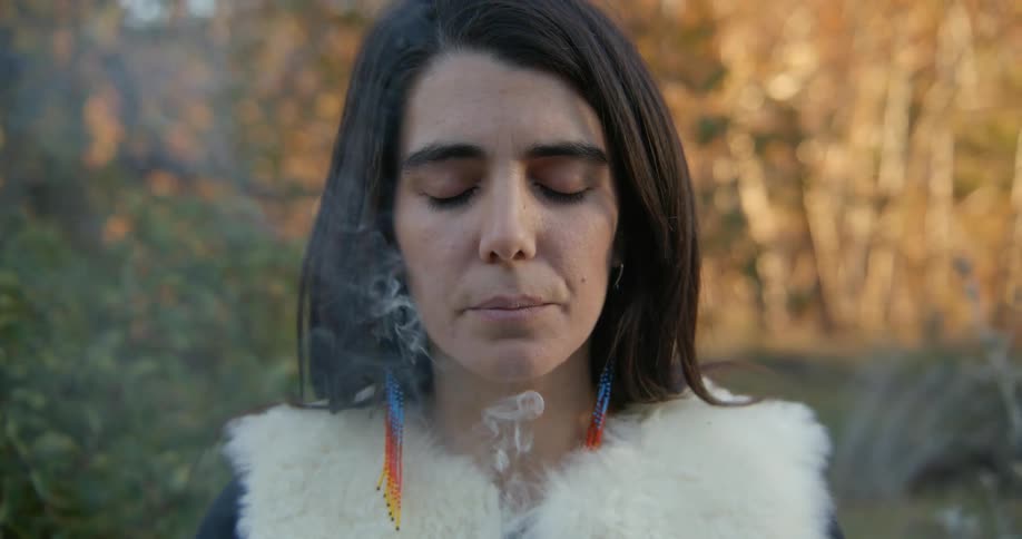 Close up of the face of a woman looking at the camera smelling incense in nature