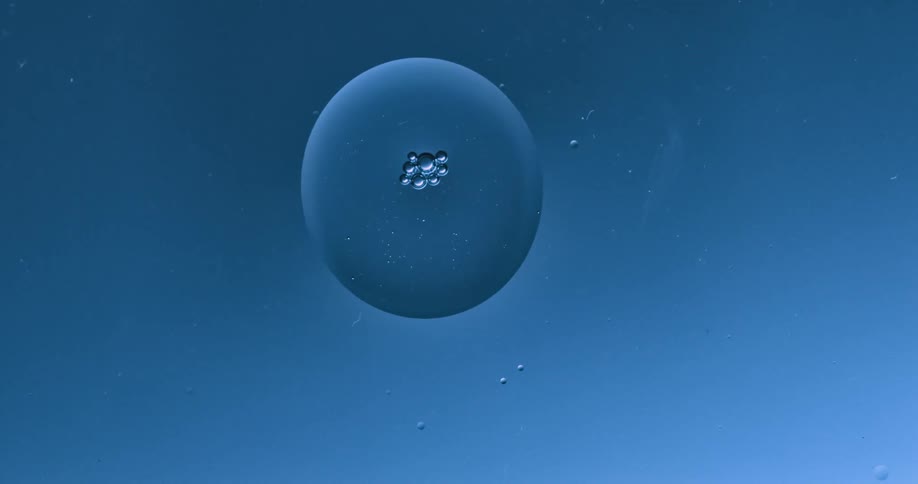 Two spheres are floating among bubbles and they touch and merge into one orb
