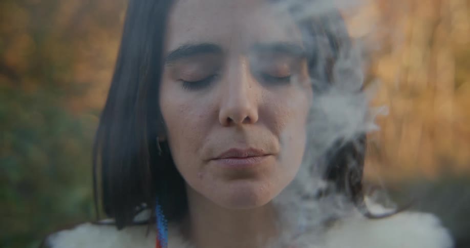 Woman wearing fur breathes in smoke with her eyes closed