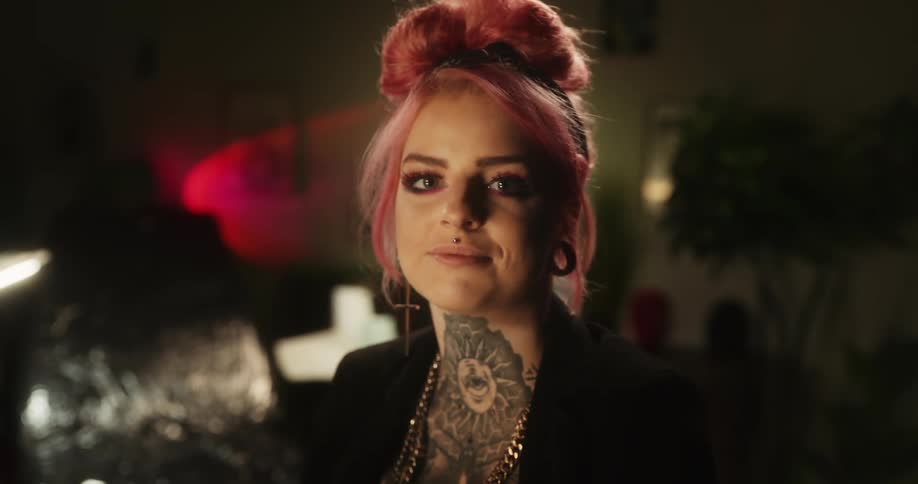 Close up of the face of a tattooed woman with colorful pink hair looking at the camera