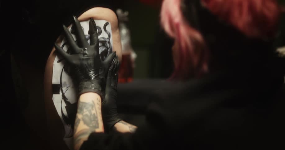 A tattoo artist is transferring the image of medusa on a mans arm