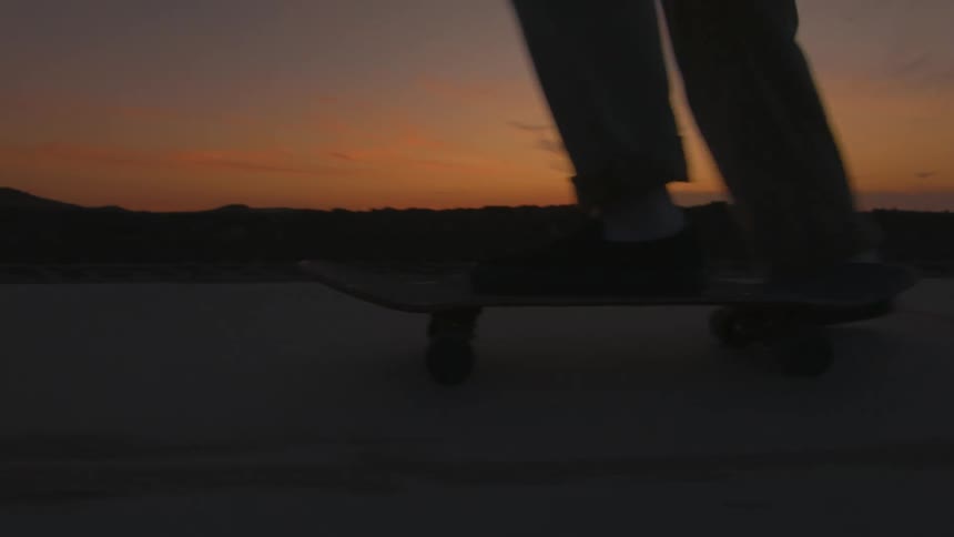 Skateboarder rides skateboard past hills silhouetted against a red sky